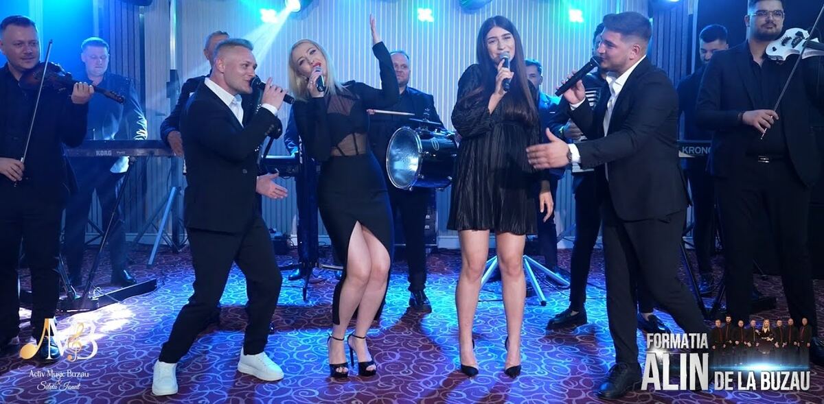 Formația pe scenă, cu soliste și instrumentiști, în lumini albastre de concert